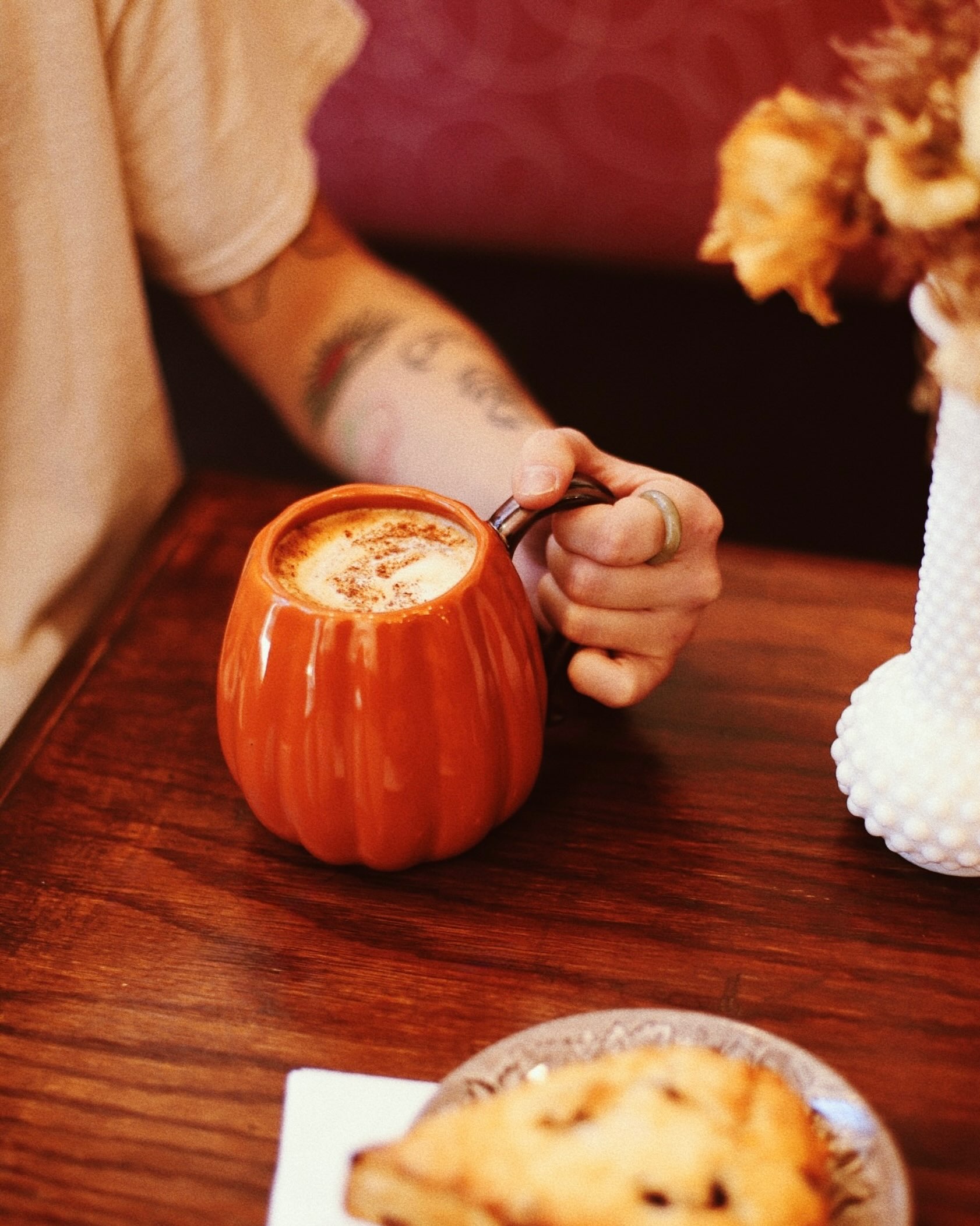 A warm drink in an orange pumpkin-shaped mug on a wooden café table