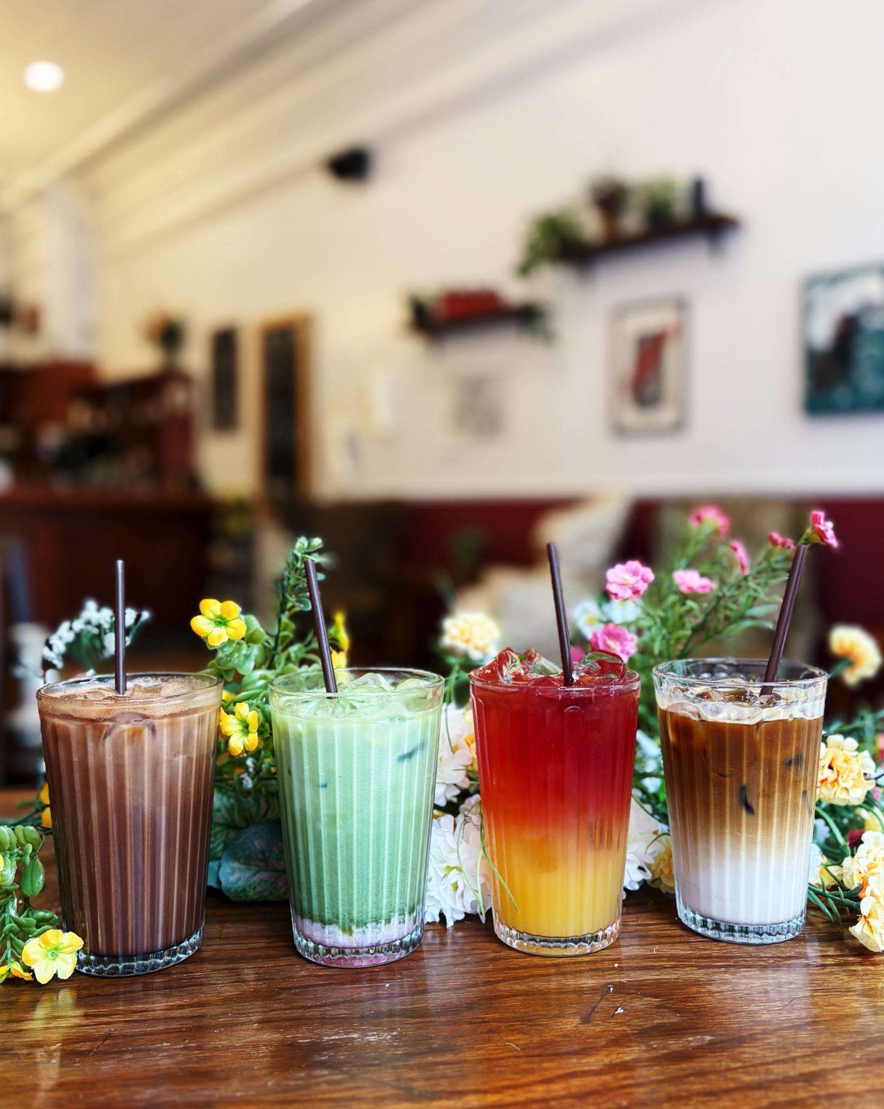 Four colourful iced seasonal drinks surrounded by flowers inside Our Place Coffeehouse